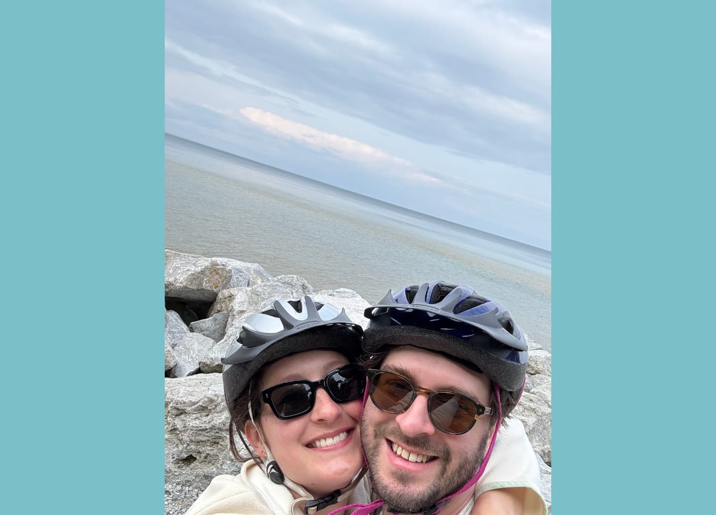 Photo of a couple wearing sunglasses and bike helmets with the lake in the background